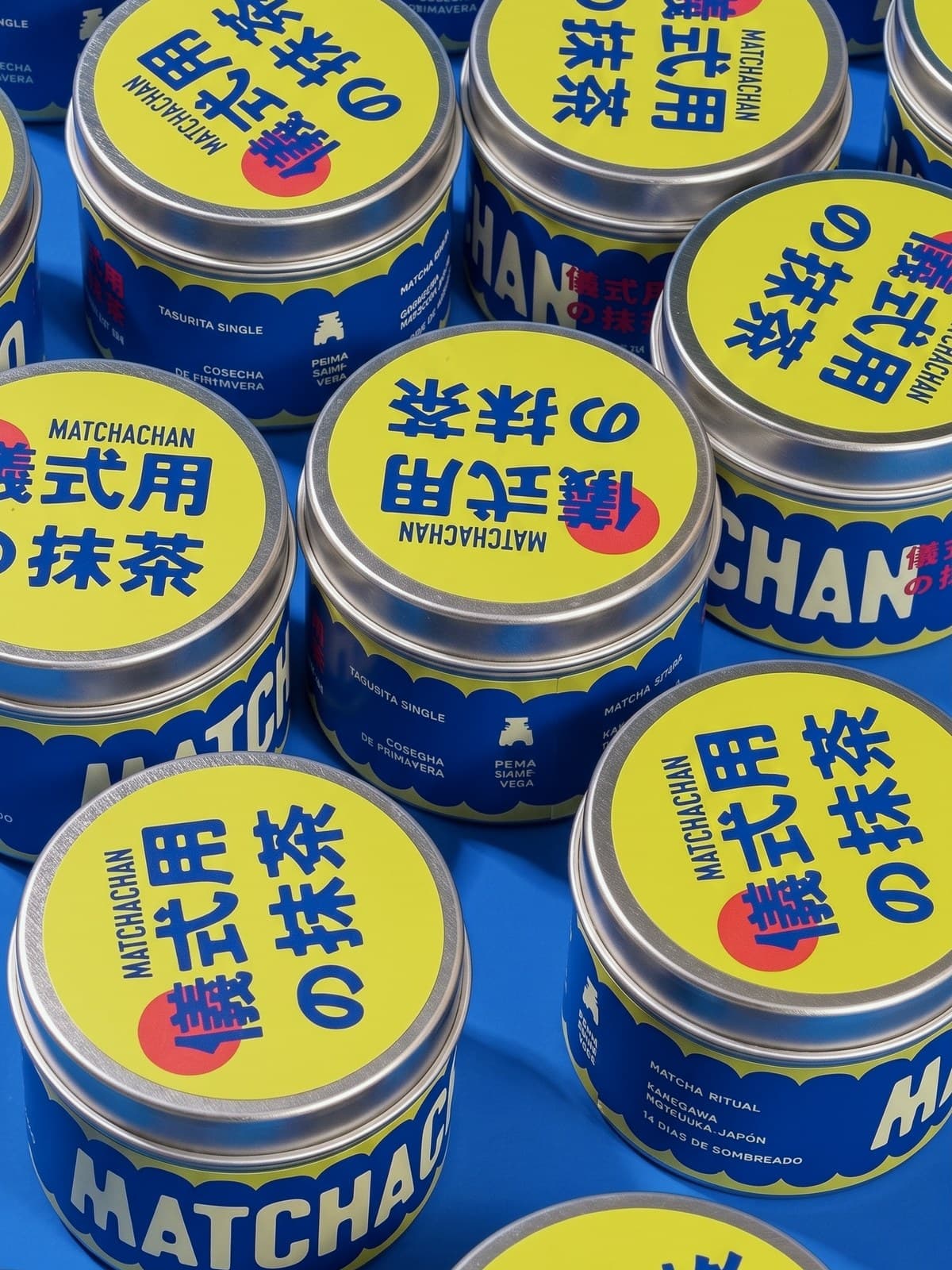 Latas de Matchachan sobre fondo azul, con la tapa amarilla y el sello de Matcha Chan